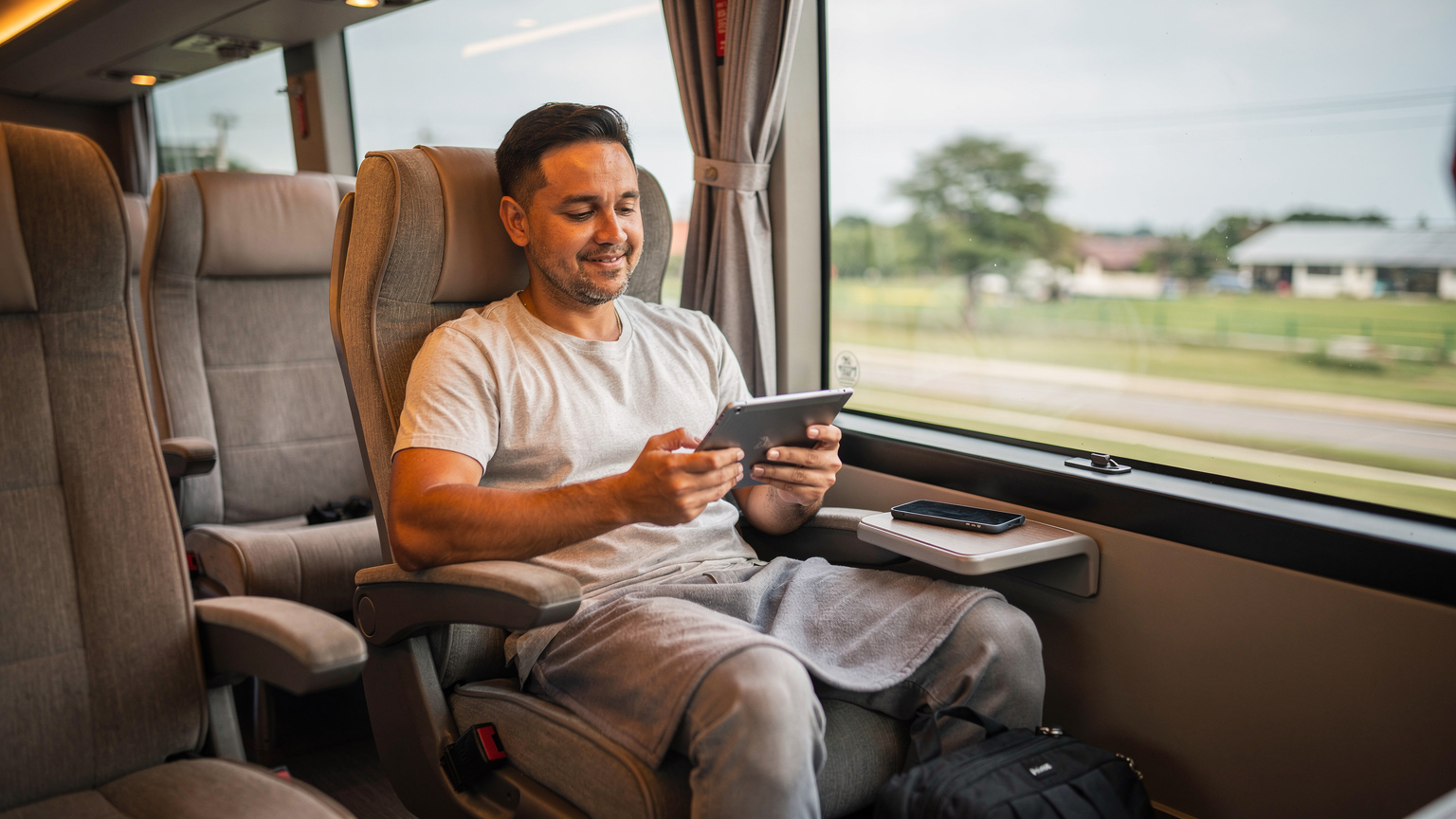 Un viaggiatore sul pullman VIP della Greenbus tra Chiang Mai e Bangkok, guarda un film scaricato sul suo tablet mentre lo smartphone è appoggiato accanto.